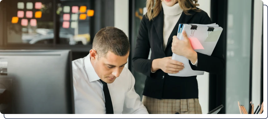 une femme debout qui regarde un homme assis travailler