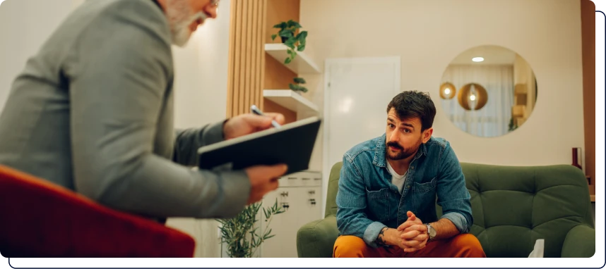 un homme qui écrit sur sa table avec un homme à ses côtés qui le regarde